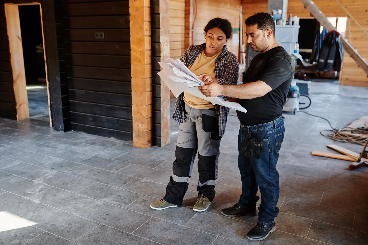Two contractors reading plans in a room being remodeled